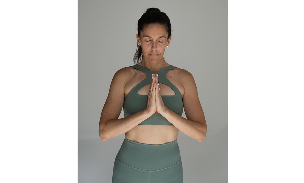 Standing in a prayer pose, I center myself—hands at heart, grounded in breath and intention. Dressed in soft green tones against a calm, neutral background, this moment reflects strength, stillness, and the quiet power of presence